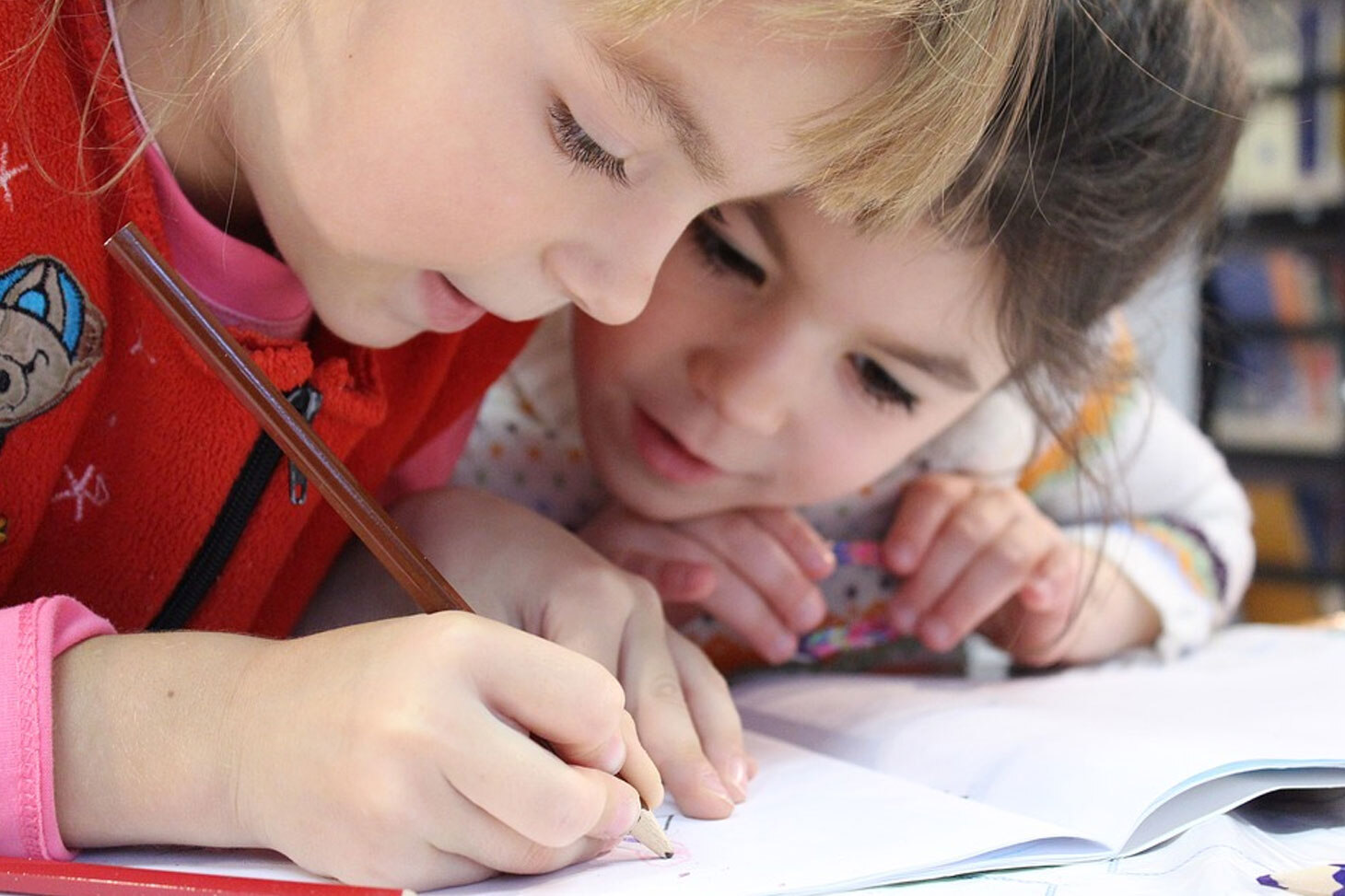 2 girls sitting together over a book and writing