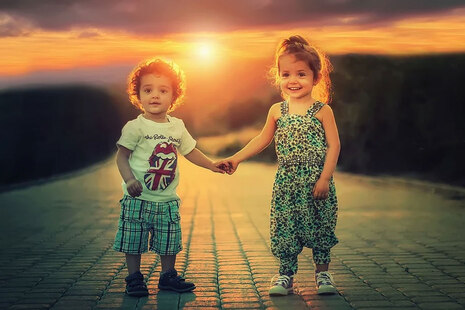 2 Kinder stehen Hand in Hand vor Sonnenuntergang